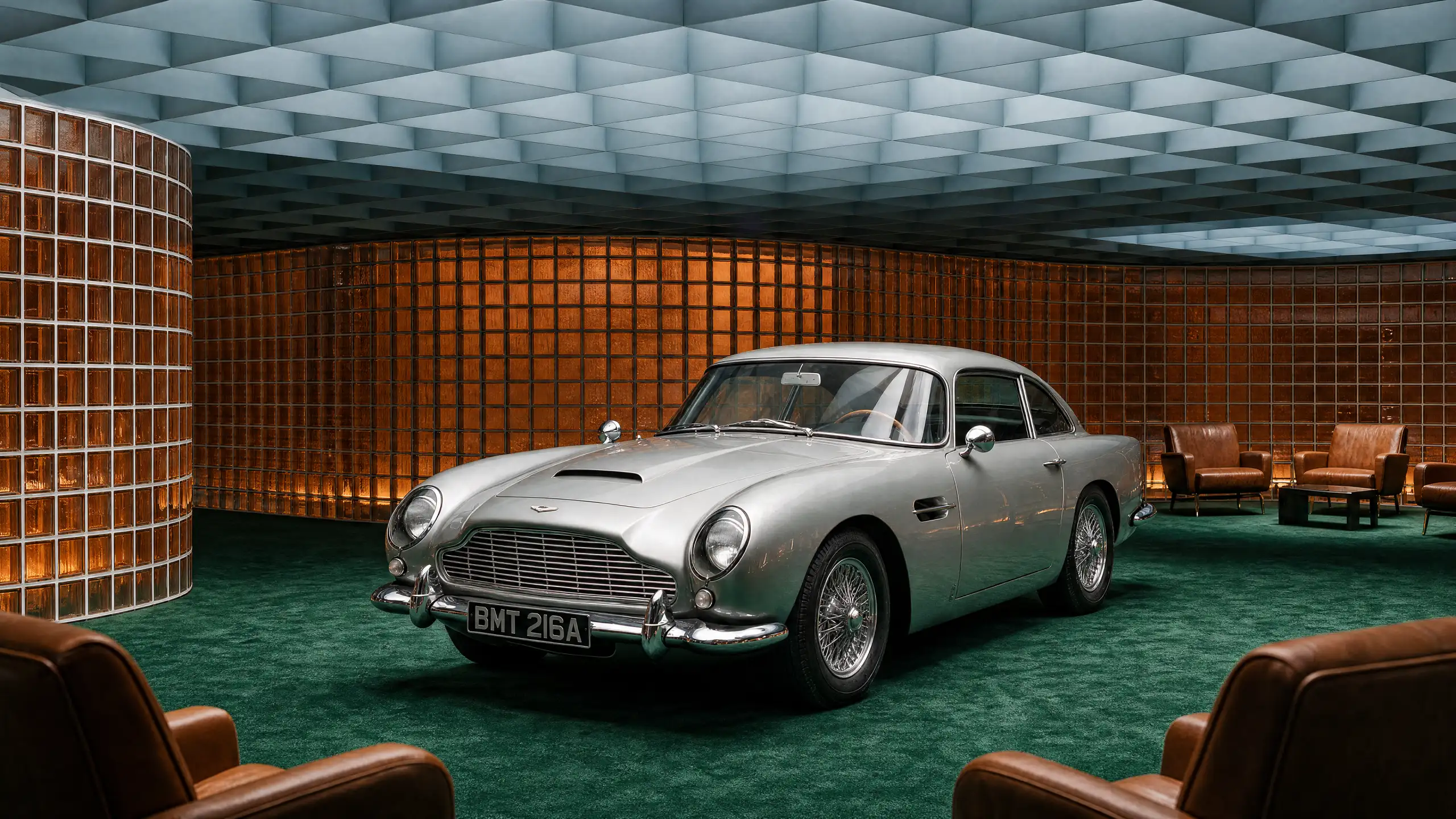 A silver Aston Martin DB5 in a showroom with an amber glass-block wall, a green carpet and brown leather armchairs